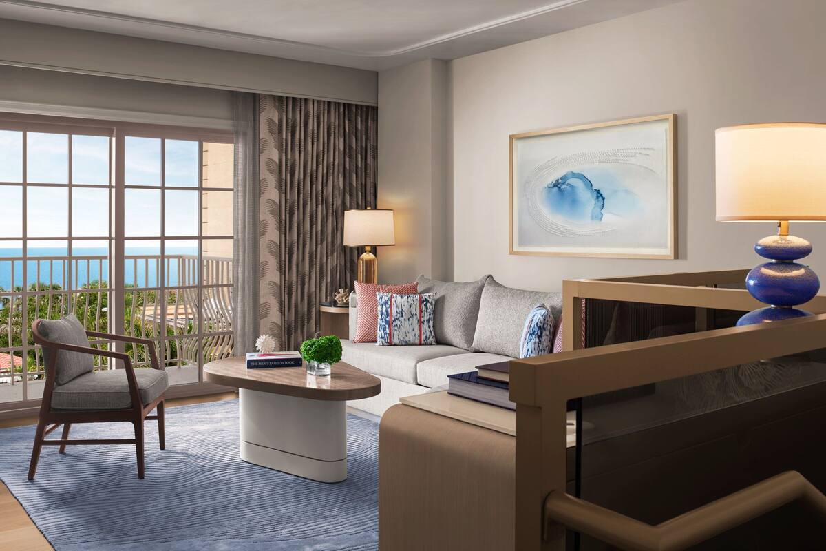 Ein modernes Hotelzimmer mit Balkon, einer Couch, einem Sessel, einem Couchtisch und einer Lampe.