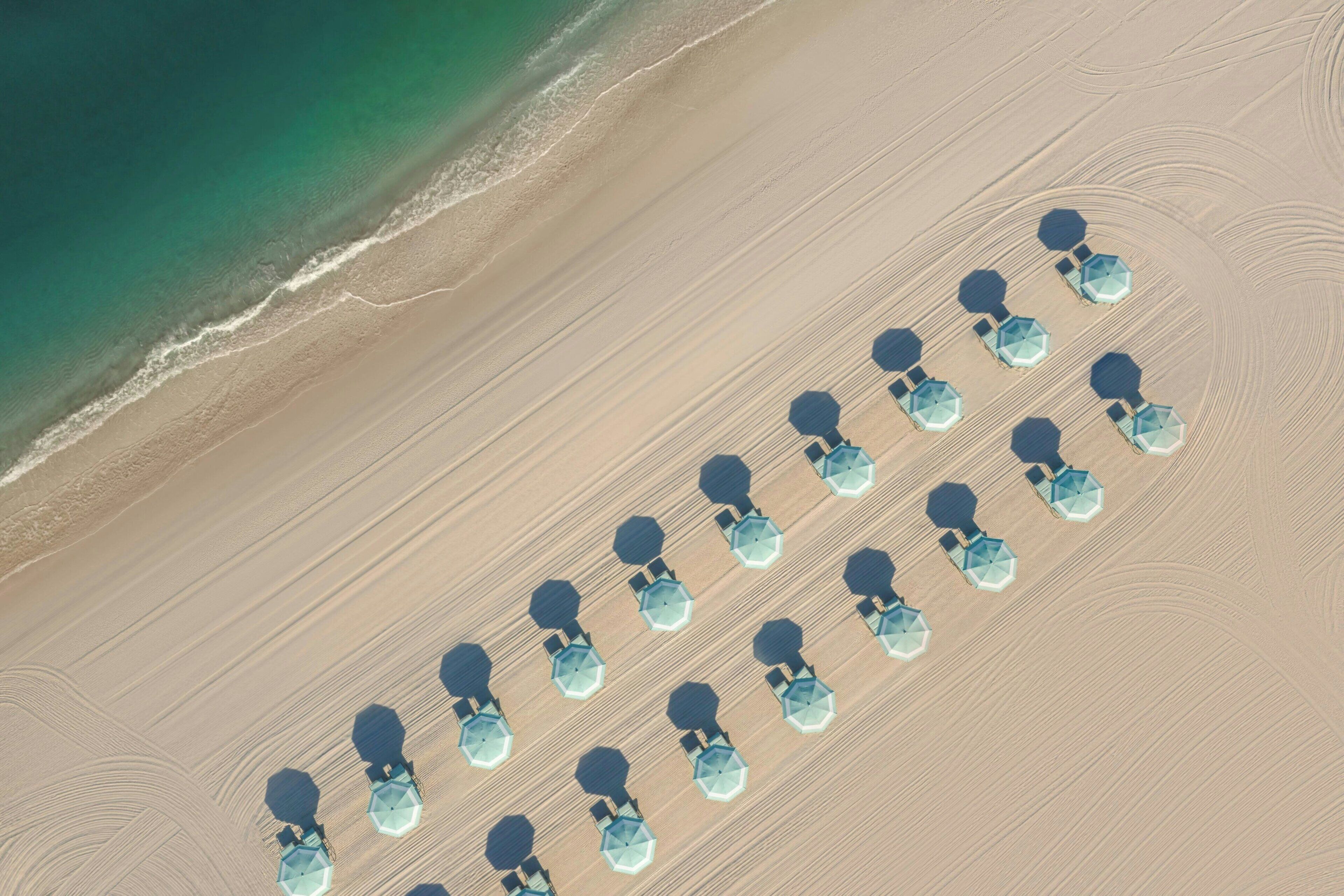 Vista aérea de una playa con hileras de sombrillas hexagonales y sillas de descanso dispuestas en un patrón.