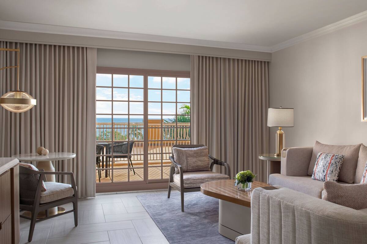 Ein Hotelzimmer mit Balkon, einer Couch, einem Sessel, einem Tisch und einer Lampe.