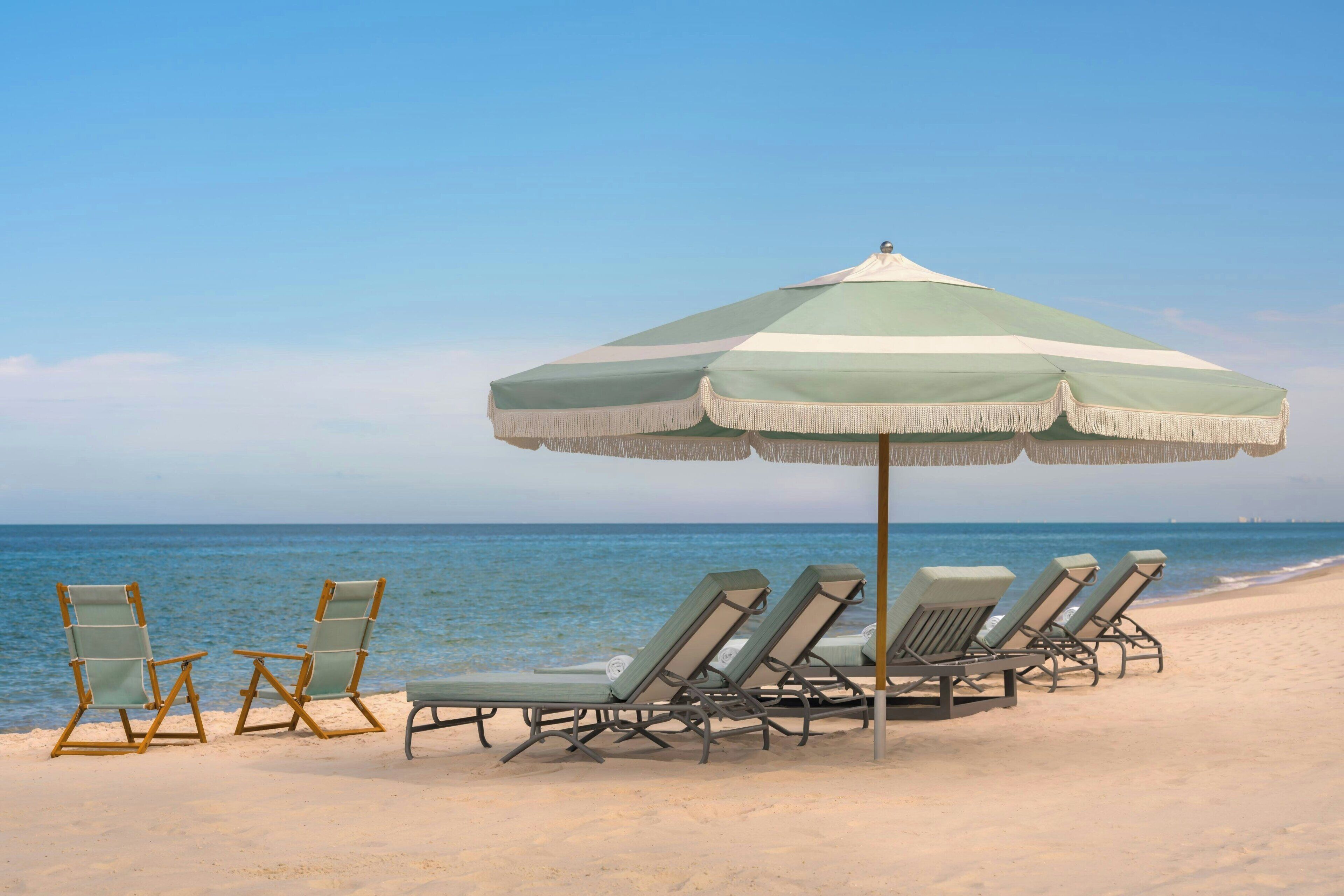 A beach with lounge chairs and a large umbrella.