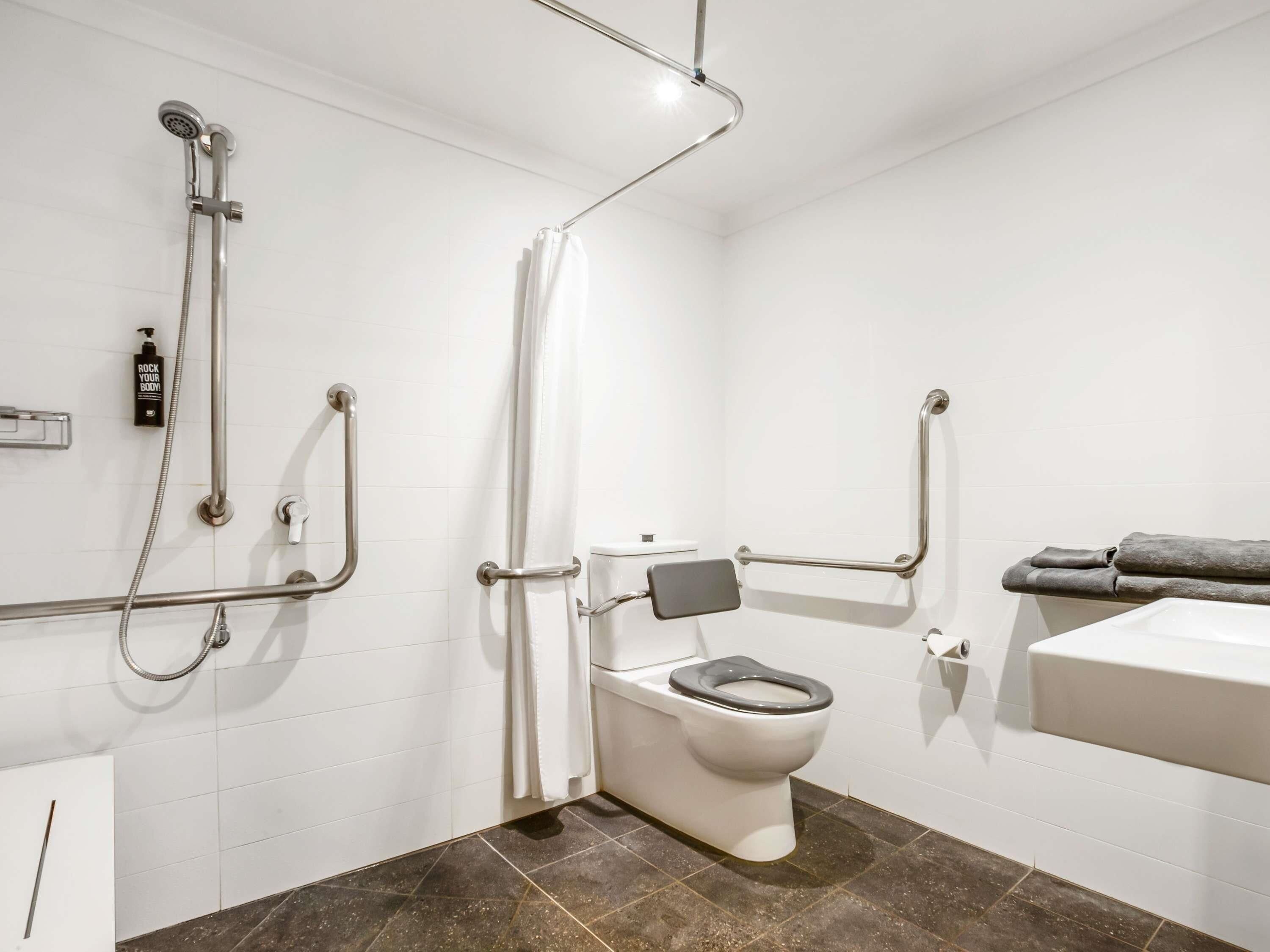 A bathroom with a white toilet, a shower with grab bars, a towel rack, and a sink with a towel.