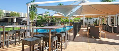 Un área de piscina al aire libre con sillones de descanso y sombrillas, rodeada por una cerca.
