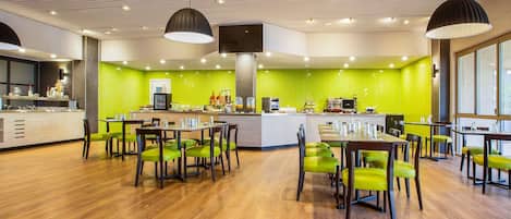 Un restaurante moderno con una pared verde en patrón espiga, suelo de madera y sillas verdes.