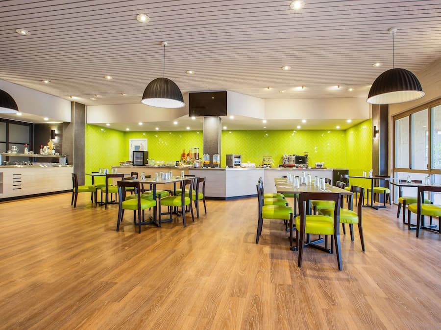 Un restaurante moderno con una pared verde en patrón espiga, suelo de madera y sillas verdes.