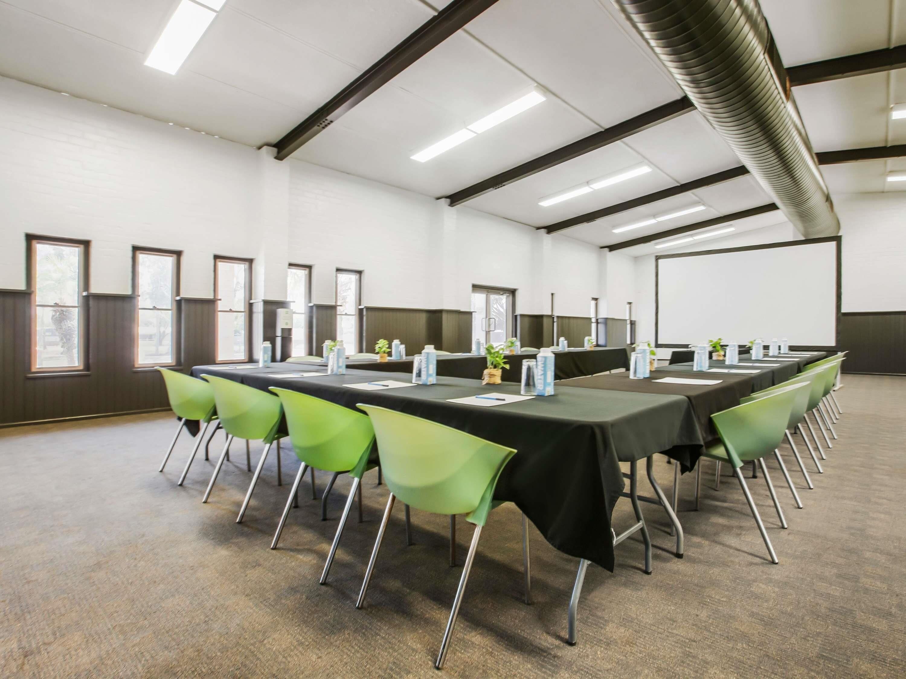 A conference room with a long table, green chairs, and a projector screen.