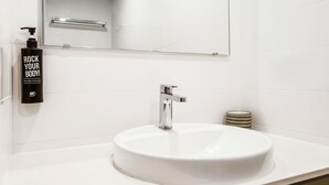 A bathroom with a white sink, a mirror, a faucet, and a bottle of body wash. - ibis Styles Karratha (Karratha)