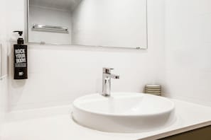 A bathroom with a white sink, a mirror, a faucet, and a bottle of body wash. - ibis Styles Karratha (Karratha)