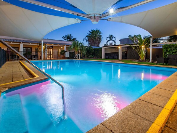 Una piscina con vista despejada del entorno, que incluye una zona de estar cubierta y un edificio con un letrero.