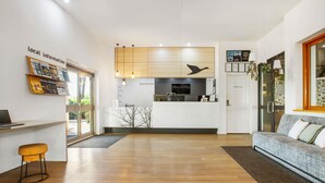 Un hall d’hôtel moderne avec un comptoir d’accueil, un canapé, un coin repas et une cuisine en arrière-plan.