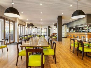 A spacious dining area with wooden tables and bright green chairs, a bar with a patterned backsplash, and large pendant lights. - ibis Styles Karratha (Karratha)