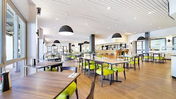 Un comedor amplio con mesas de madera y sillas verdes, una barra al fondo y un diseño de techo moderno.