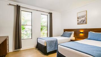 A hotel room with two beds, a wooden headboard, a nightstand, a desk, and a window with curtains.