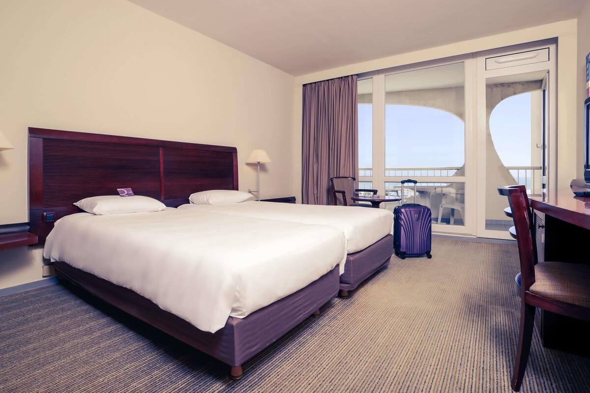 A hotel room with a large bed, a desk, a chair, and a view of the balcony.