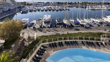 A marina with numerous boats docked, a swimming pool with sun loungers, and a large building with balconies.