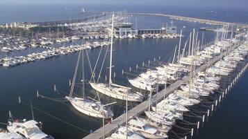 Un puerto deportivo con numerosos barcos amarrados en fila, un muelle que se extiende hacia el agua y una vista distante de la costa.