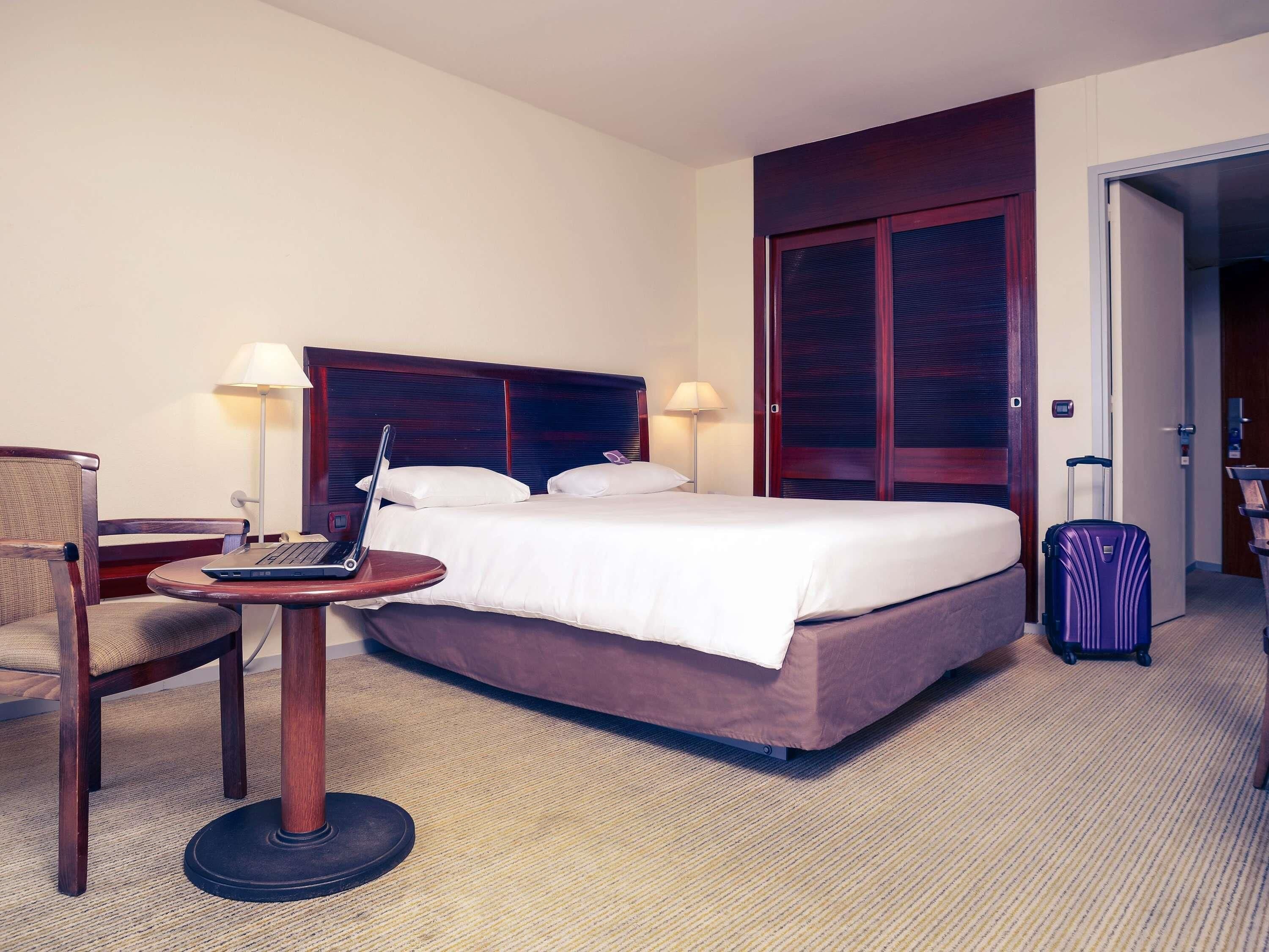 Een hotelkamer met een bed, een bureau met een laptop, een stoel, een koffer en een kledingkast.