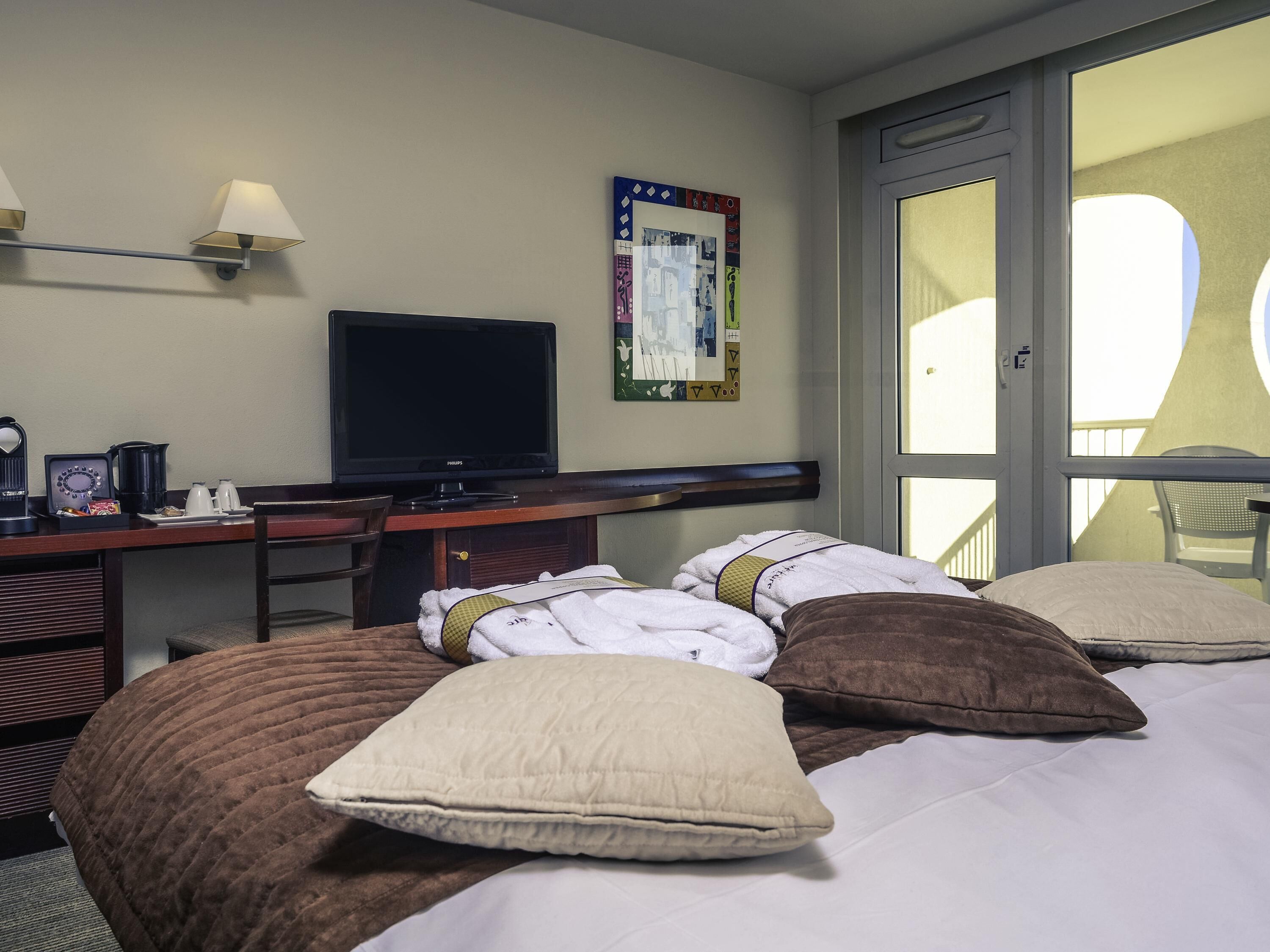 A hotel room with a bed, a desk with a television, a chair, and a window.