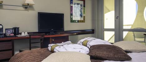 A hotel room with a bed, a desk with a television, a chair, and a window.