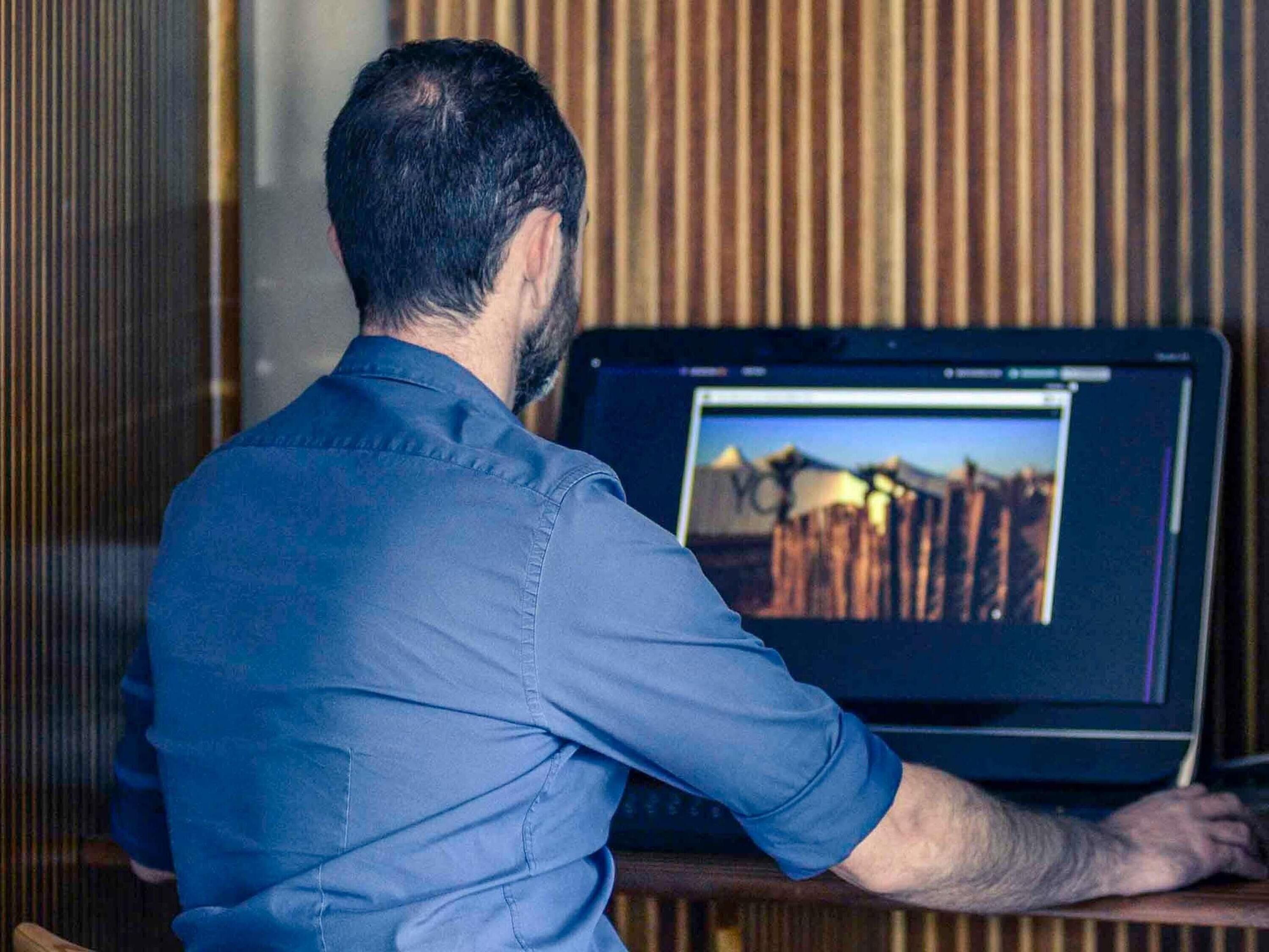 A person sitting at a desk with a laptop displaying a landscape image.
