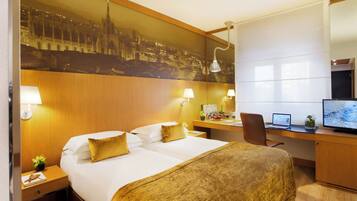 Quarto de hotel com cama, escrivaninha, computador e um grande mural com vista para a cidade.