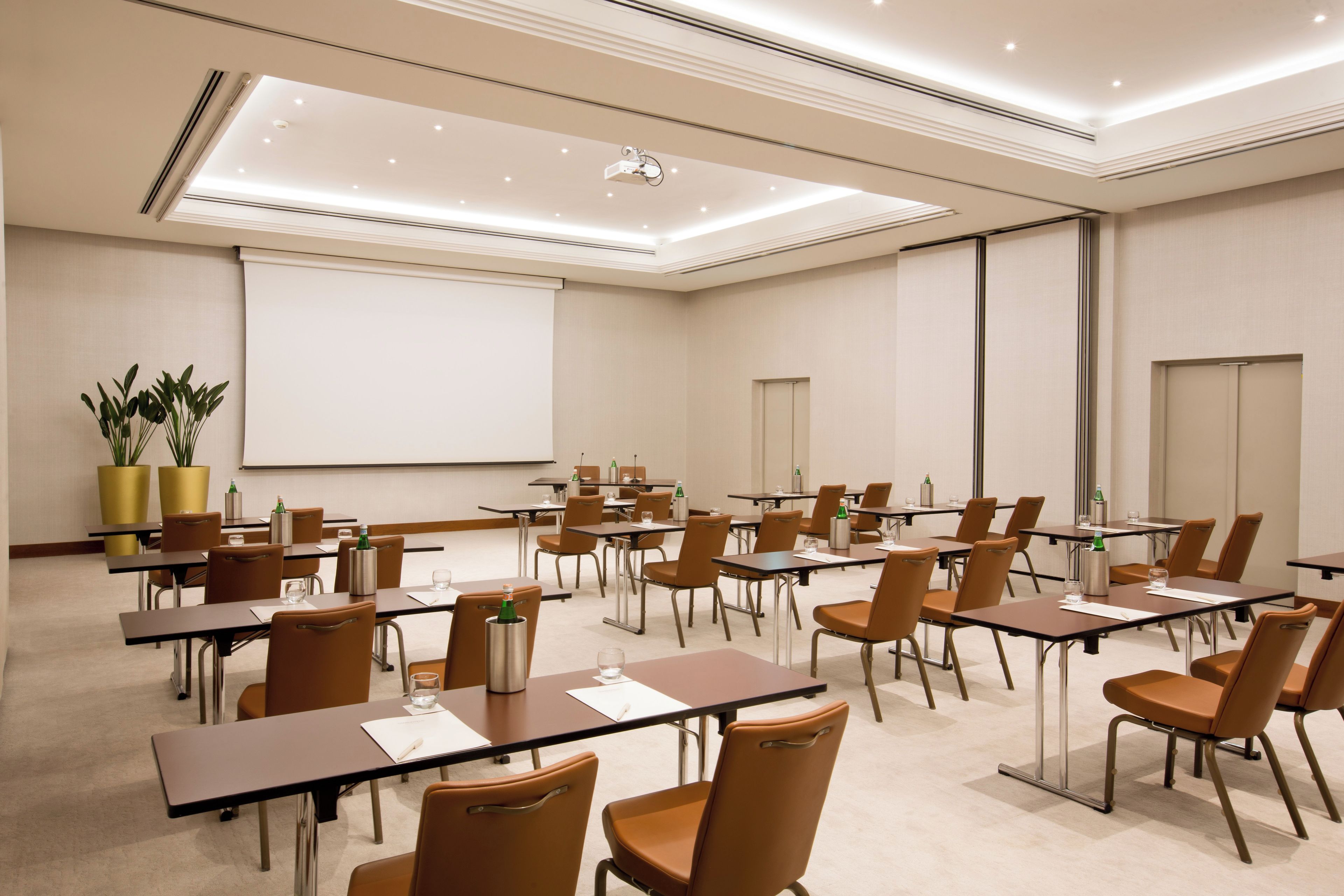 Un salón de conferencias con mesas y sillas, una pantalla de proyector y una pizarra.