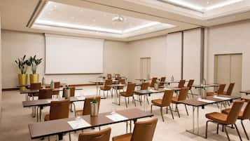 Un salón de conferencias con mesas y sillas, una pantalla de proyector y una pizarra.