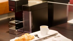 A coffee machine, a cup of coffee, a croissant, and a laptop on a wooden table. - Starhotels Tourist (Milan)