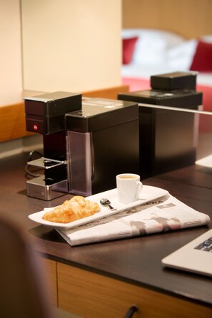Une machine à café, une tasse de café, un croissant et un ordinateur portable sur une table en bois.