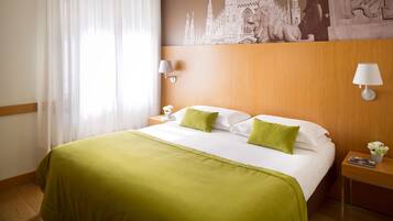 Una camera d'albergo con un letto grande, cuscini verdi, una testiera in legno, un comodino con una lampada e un affresco sulla parete.