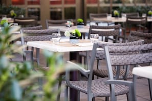 A restaurant setting with wicker chairs and tables, each with a small vase and a glass. - Starhotels Tourist (Milan)
