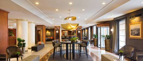 A hotel lobby with a round table, bar, seating area, and a large window.