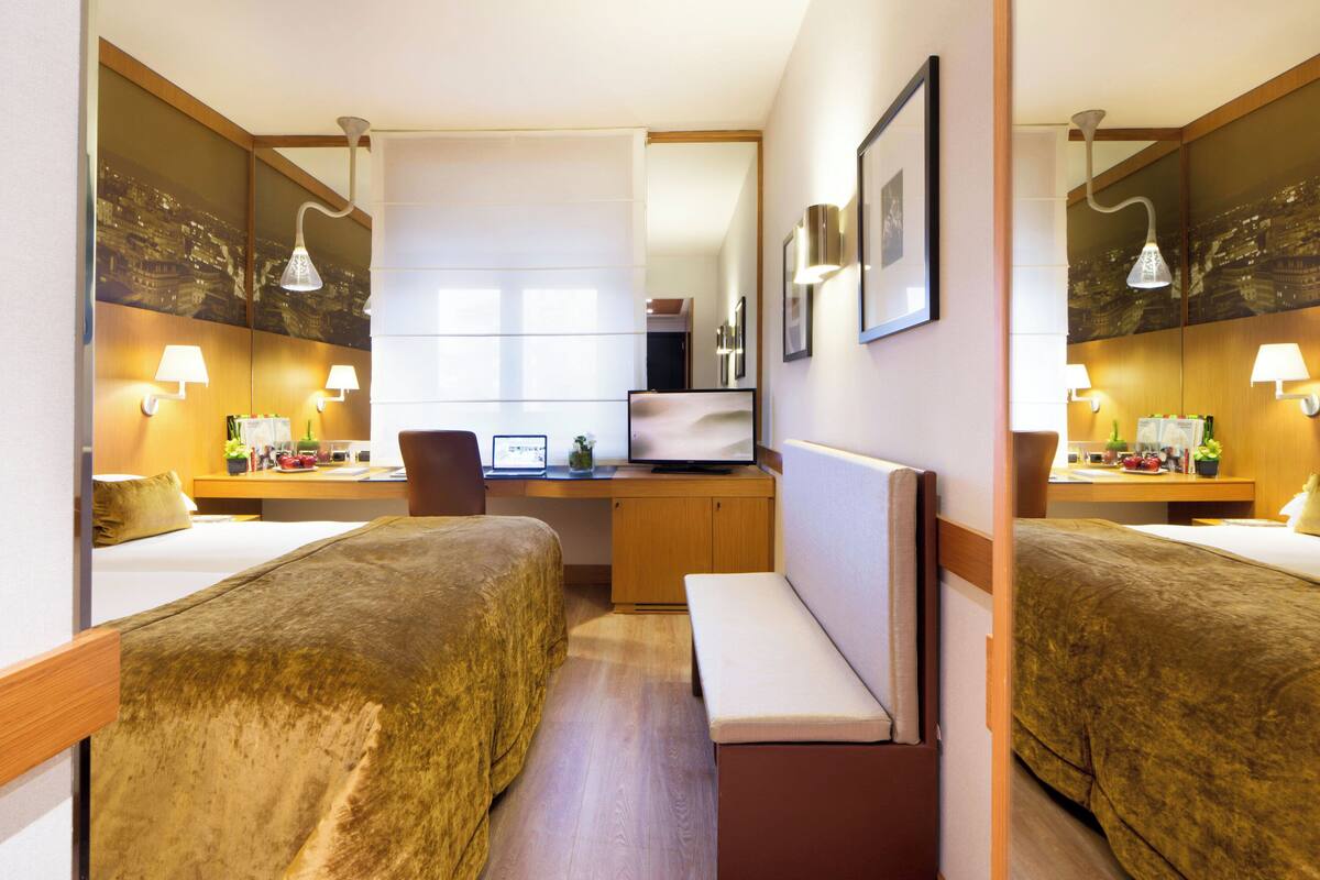 A hotel room with two beds, a desk, a chair, a TV, and a mirror.