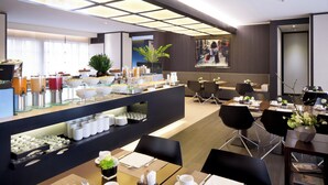 Un espace repas moderne dans un hôtel, avec un buffet, des tables et des chaises, et un grand tableau accroché au mur.