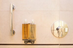 Une salle de bain avec un pommeau de douche chromé, deux flacons de lotion pour le corps de la marque Stannotel et un robinet rond chromé.