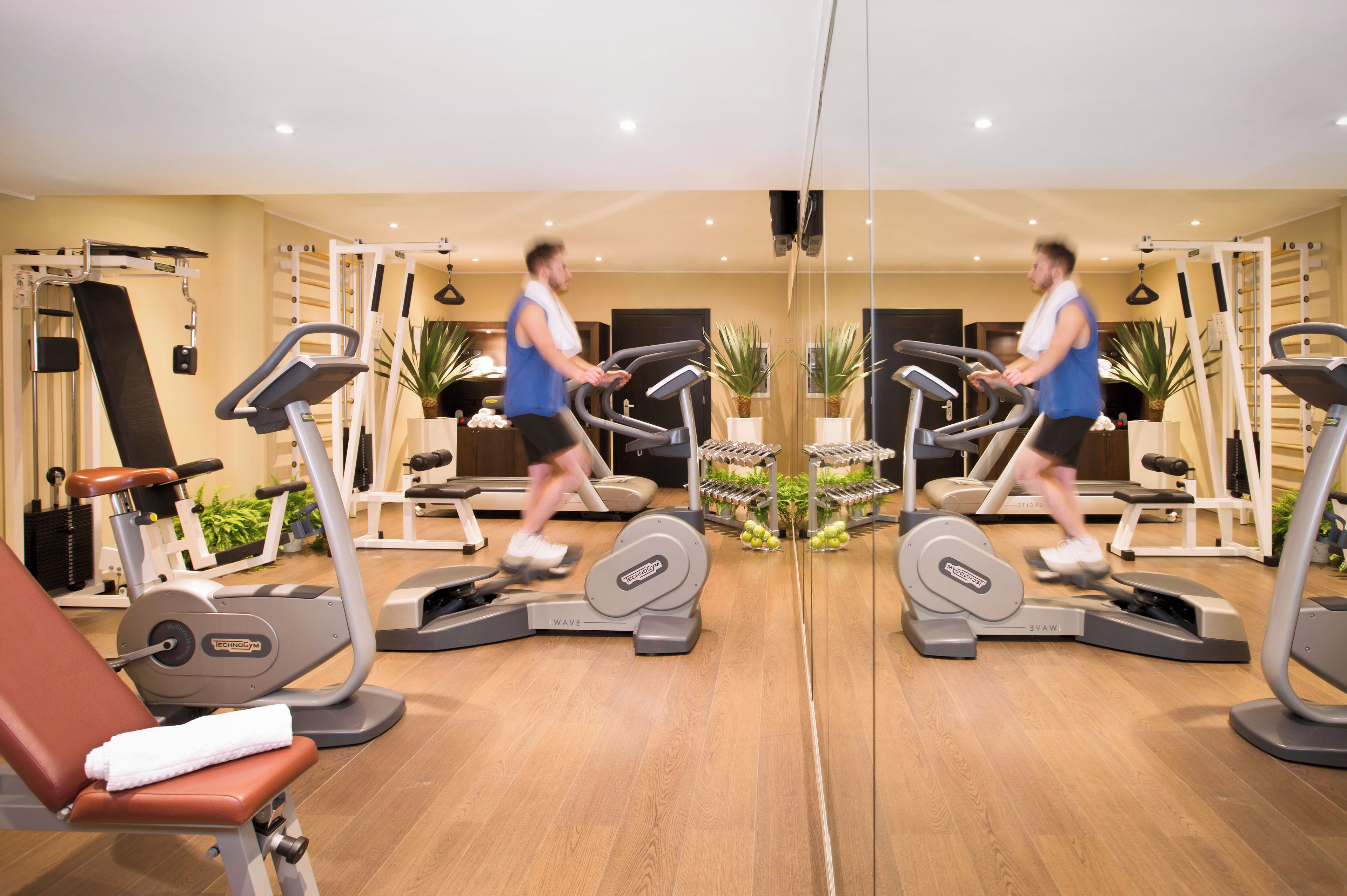 Un gimnasio con cintas de correr, máquinas de pesas y un espejo que refleja el espacio.
