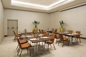 A conference room with multiple tables and chairs, equipped with water bottles and glasses, and two potted plants. - Starhotels Tourist (Milan)