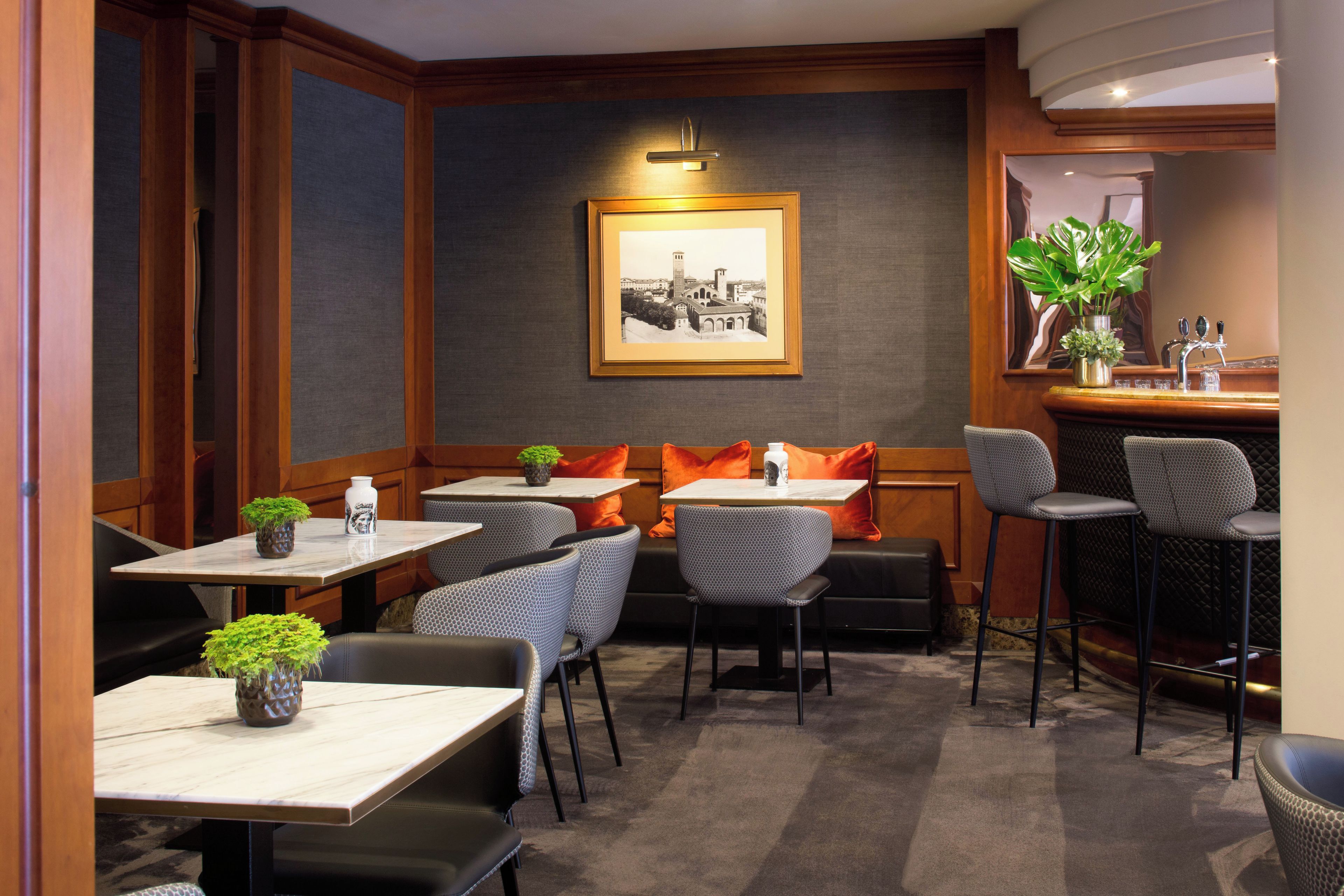 Interior de un restaurante con varias mesas y sillas, una zona de bar y un cuadro en la pared.