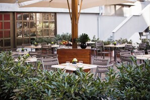 An outdoor dining area with multiple tables and chairs, surrounded by greenery. - Starhotels Tourist (Milan)