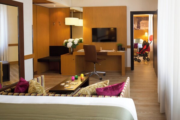 Une chambre d’hôtel avec un lit, un bureau, une chaise, une télévision et une petite table sur laquelle est posé un vase de fleurs.