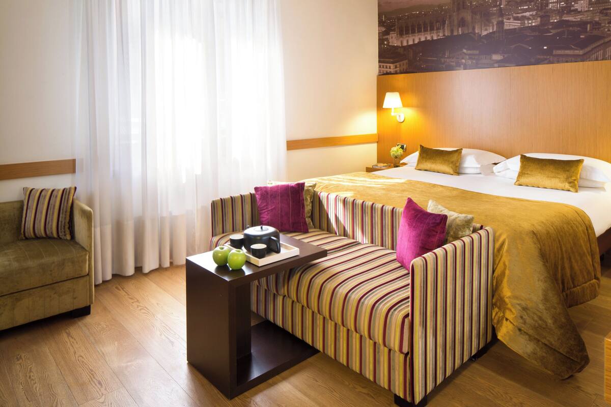 Une chambre d’hôtel avec un lit, un canapé, une table basse et une vue sur la ville.