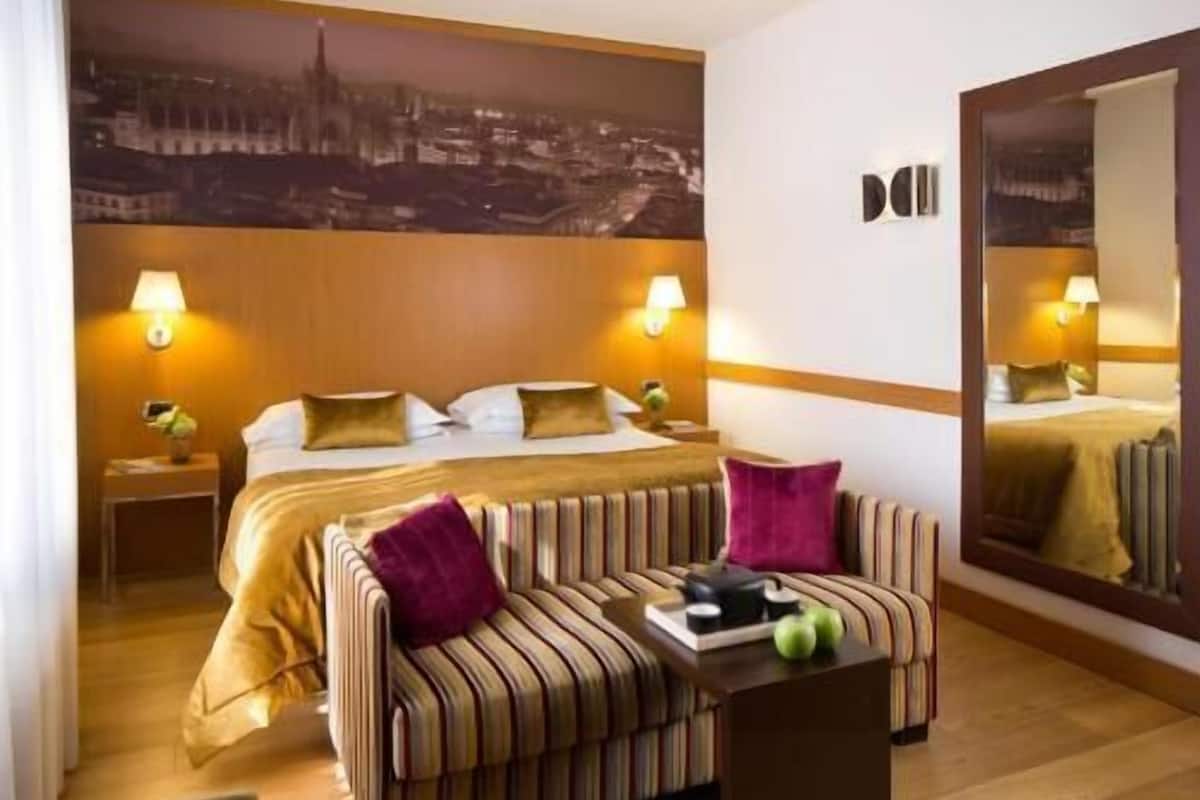 A hotel room with a bed, a sofa, a small table, and a large mirror.