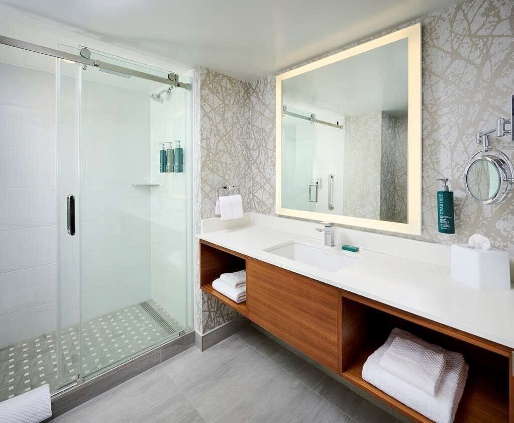 Un baño moderno con cabina de ducha de vidrio, un espejo grande y un mueble de tocador de madera con lavabo.