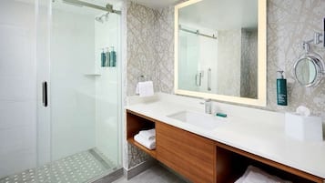 Un baño moderno con cabina de ducha de vidrio, un espejo grande y un mueble de tocador de madera con lavabo.