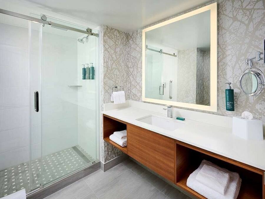Un baño moderno con cabina de ducha de vidrio, un espejo grande y un mueble de tocador de madera con lavabo.