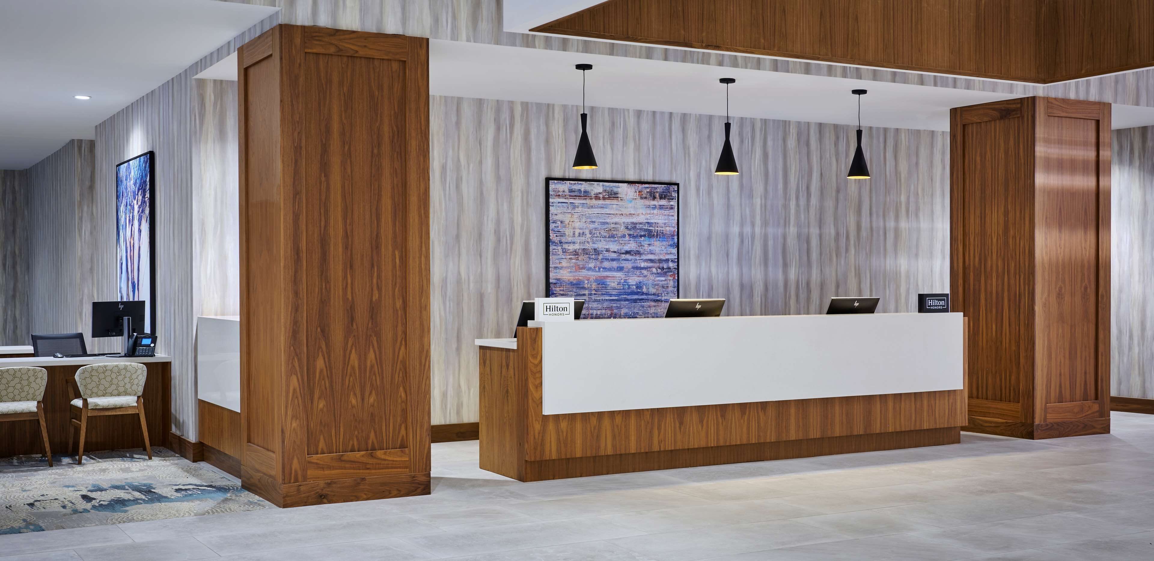 A hotel reception area with a wooden reception desk, a large abstract painting, and three pendant lights.
