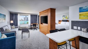A hotel room with a bed, a desk, a TV, a sofa, and a view of a cityscape.