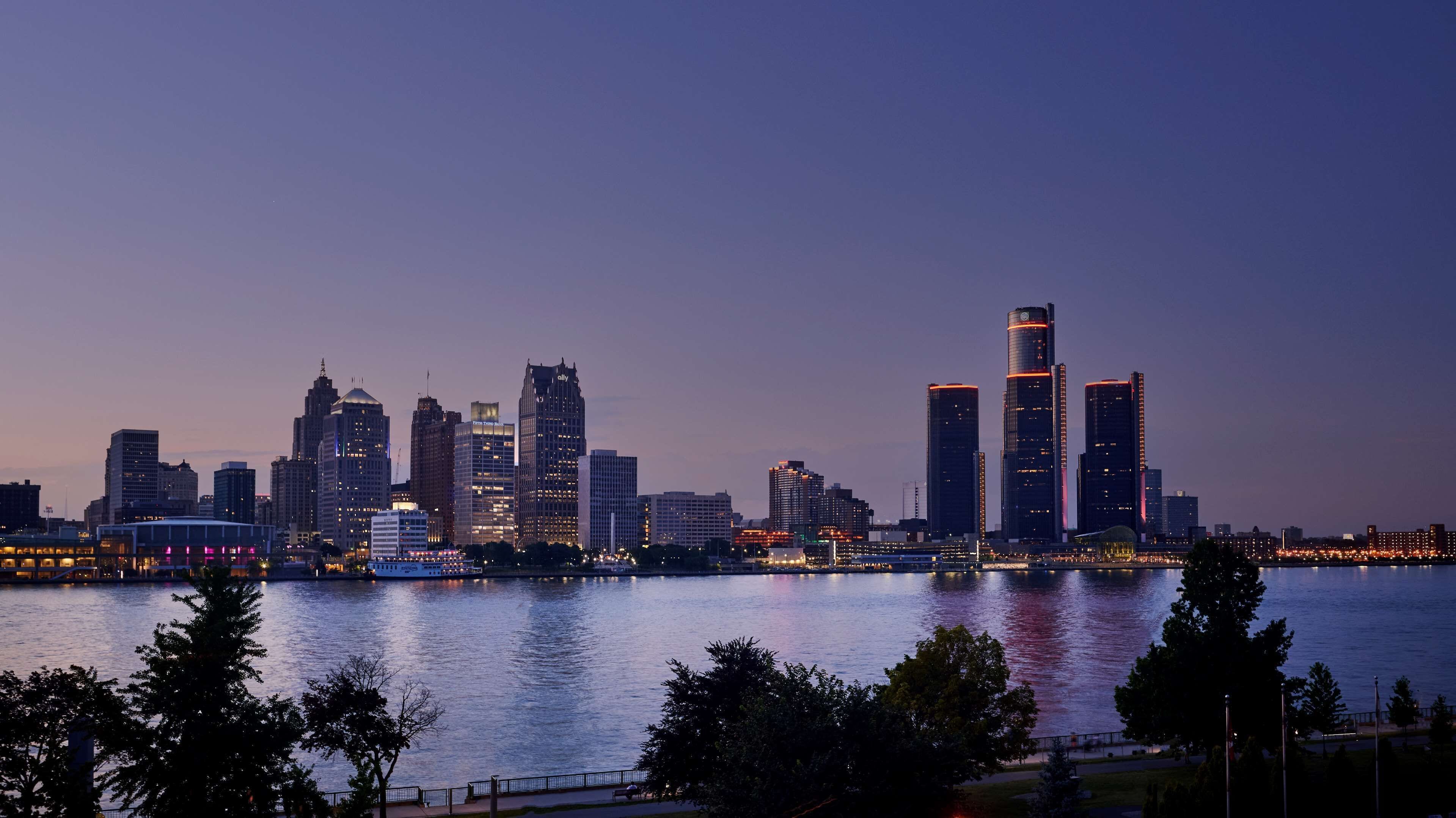 A city skyline at dusk with illuminated buildings along a waterfront.