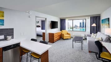 Habitación de hotel con kitchenette, comedor, sofá, sillón y un amplio ventanal con vista a la ciudad.
