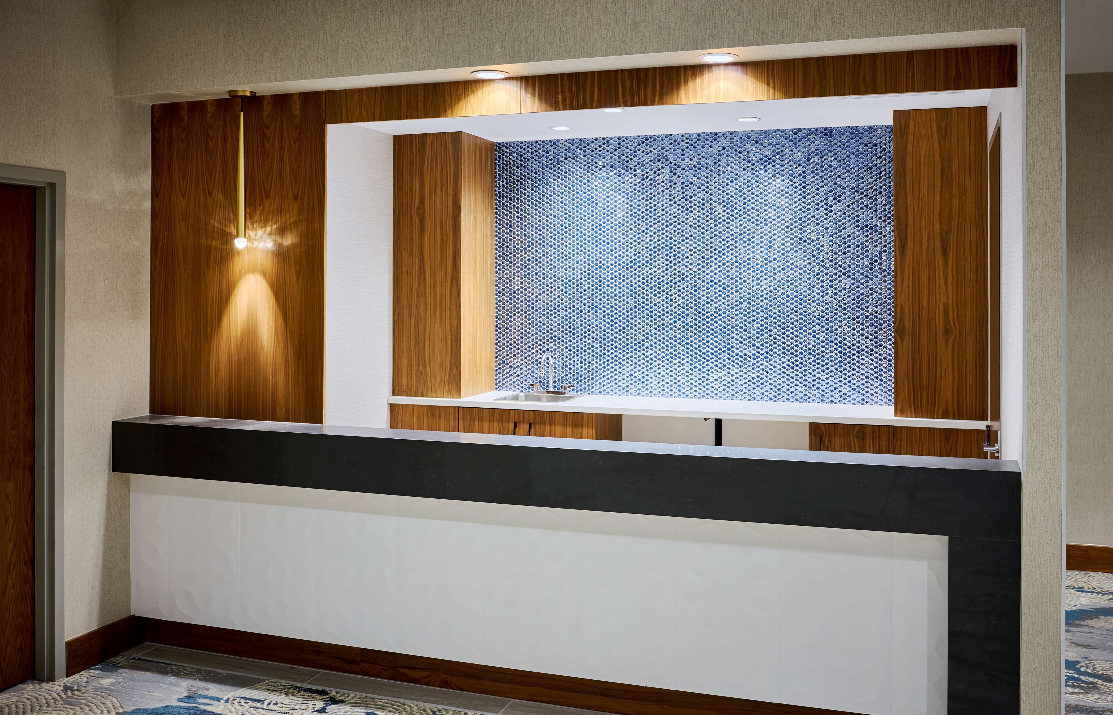 Una moderna área de recepción con paneles de madera, un separador de vidrio con diseño y luces empotradas.