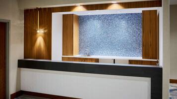 Una moderna área de recepción con paneles de madera, un separador de vidrio con diseño y luces empotradas.